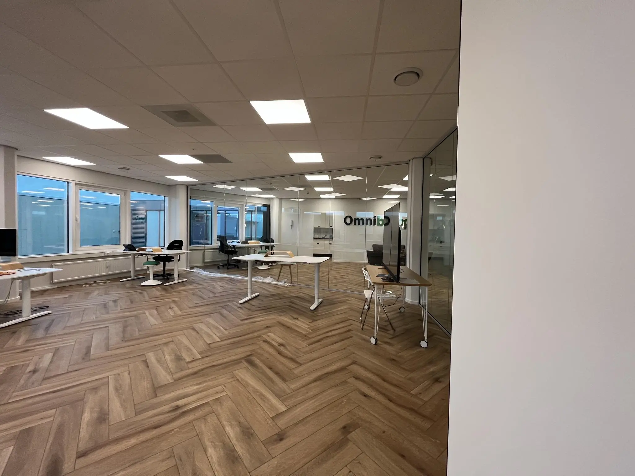 Moderne kantooruimte aan de Lange Dreef met glazen wanden, houten visgraatvloer en verstelbare bureaus.